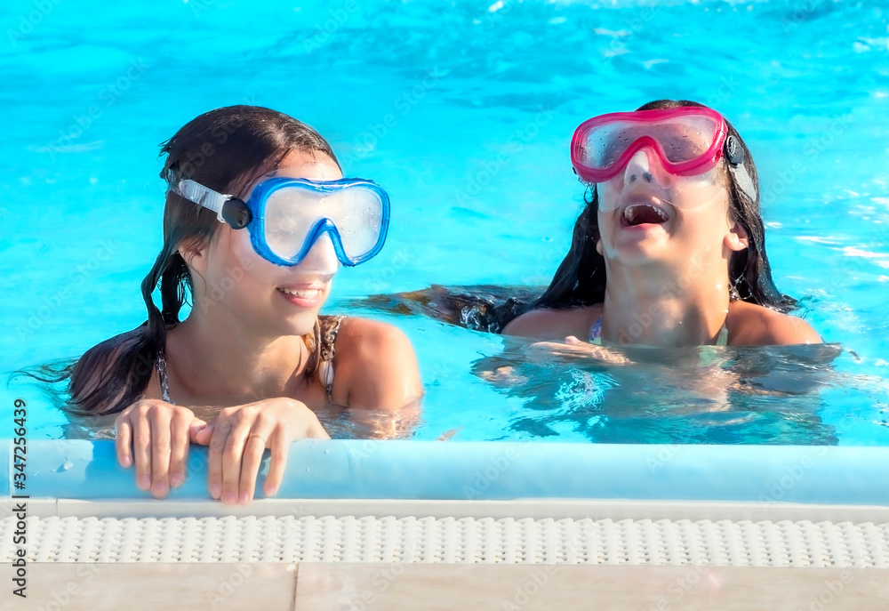 two happy teenager girls playing in the swimming pool at the day time