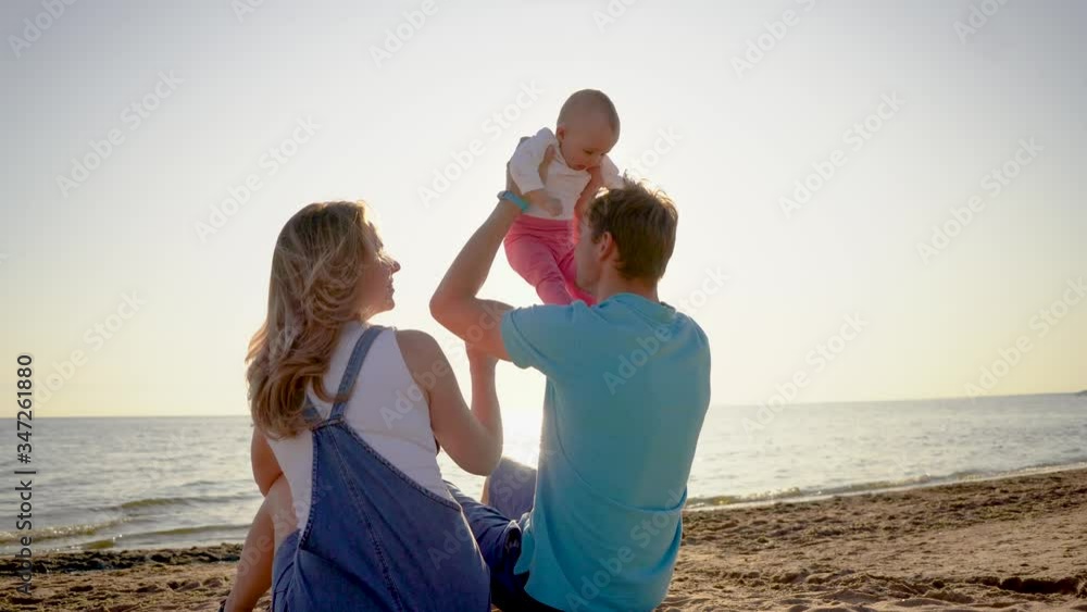 Happy family - father, mother and baby sitting on the sunset sea beach. Parents with children on summer vacations. Happy family - father, mother and baby sitting on the sunset sea beach. Parents with children on summer vacations.