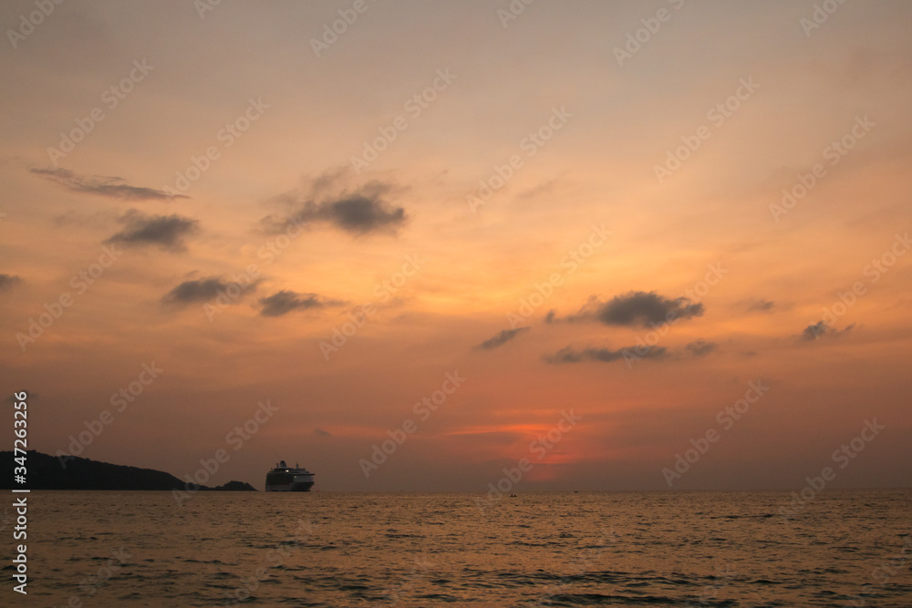 A large trade ship arrives on the shores of Thailand against the backdrop of an orange sunset. A large trade ship arrives on the shores of Thailand against the backdrop of an orange sunset.