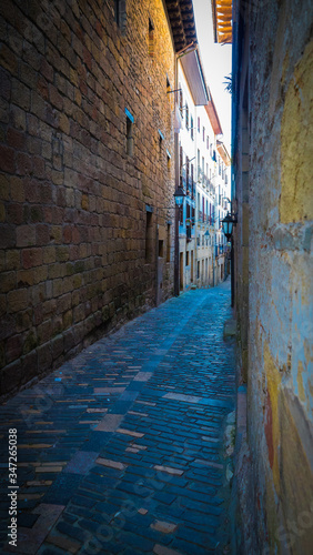 Narrow street in medieval village. Cobblestone street and stone walls, old lampposts. Basque country. © Aitor