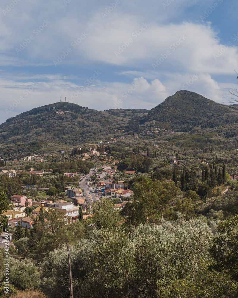 Moraitika, Corfu. Mediterranean town with forests around and hills in the background. Cloudy skies.