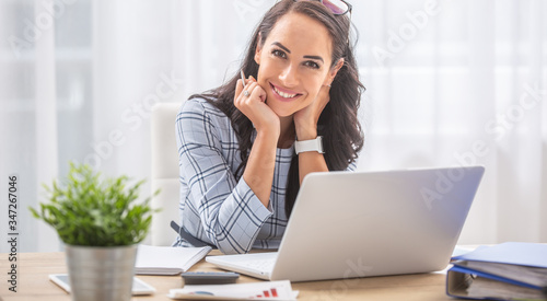 Pretty businesswoman smiles at the camera while sitting at her desk in front of the computer photo