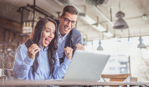 Businesswoman and businessman colleagues celebrate a success with enthusiastic facial expressions looking at the notebook screen