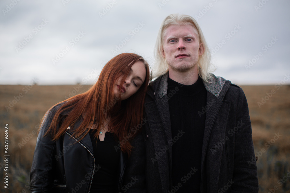 A red-haired girl is lying on the shoulder of an albino guy. The pair are standing in the field. The guy looks into the camera, the girl with his eyes closed A red-haired girl is lying on the shoulder of an albino guy. The pair are standing in the field. The guy looks into the camera, the girl with his eyes closed