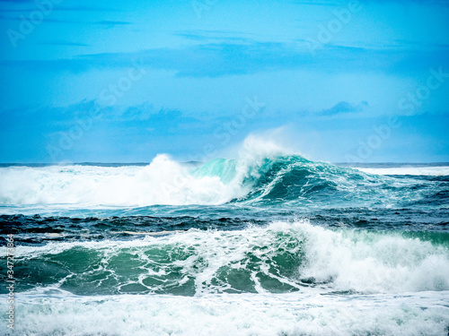 Big waves on the north shore of Oahu with aquamarine seas, white foam and blue skies.