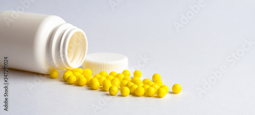 Round yellow vitamins are poured out on a white glossy table from a white plastic bottle. Concept. Place for the label. Diagnosis.