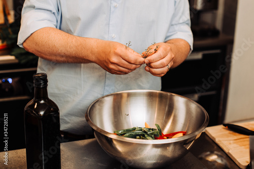 Male chef putting herbs in bell pepper while standing at a kitchen counter, crop on hands and a bowl, close up.