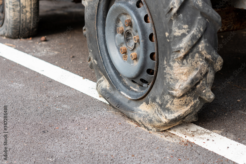 Flat tire of tractor on asphalt road, big car wheel wait for repair, maintanance in farm transportation Flat tire of tractor on asphalt road, big car wheel wait for repair, maintanance in farm transportation