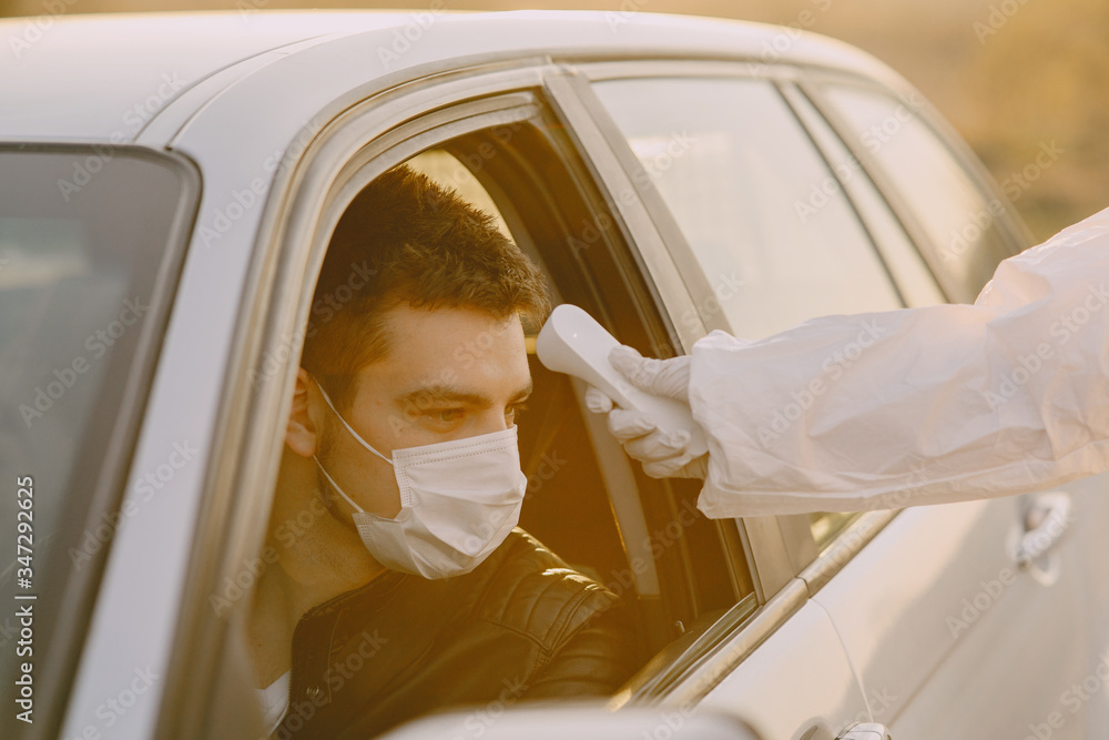 Person in a protective suit. Doctor checks the temperature in the berson behind the whell. Person in a protective suit. Doctor checks the temperature in the berson behind the whell.