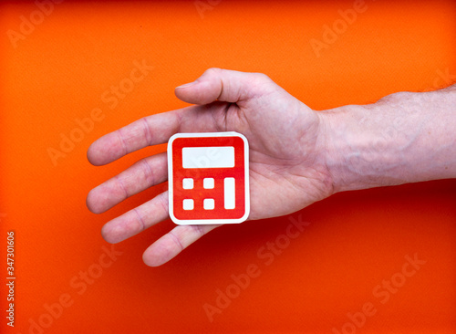 Il faut tout calculer, pictogramme imprimé de calculatrice tenu par un main d'homme, sur fond orange photo