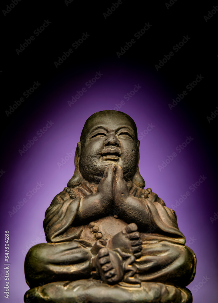 A small replica statue of The Buddha with a green background.  Purple representing divinity and immortality