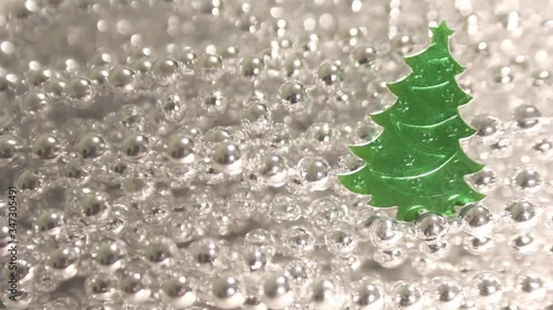 Cinemagraph of Christmas (New Year, seasonal) green confetti fir tree shaped on the background of Christmas silver beads on a string decoration