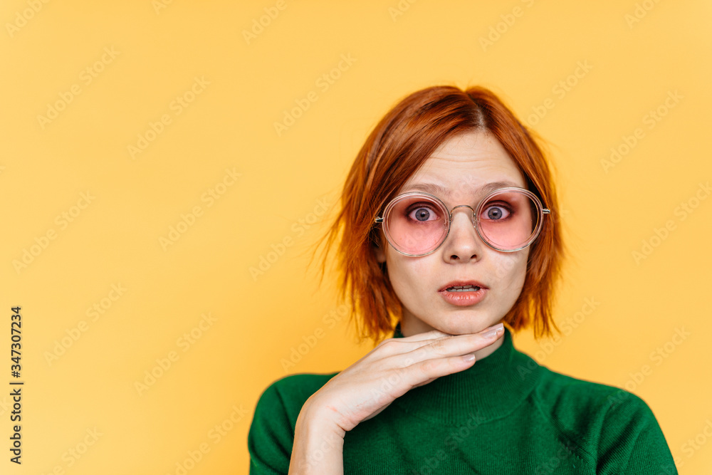 Image of surprised woman wearing glasses and dressed in green sweater over yello background. Look at camera