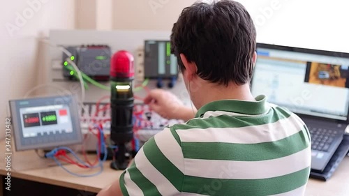 Back View of Young Man Who is Working Home Office and Making Online Education about PLC and Operator Panel Programming. Distance learning, also called distance education, e-learning or online learning