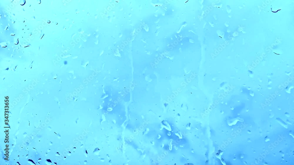 Rain drops dripping, falling down the blue window glass Rain drops dripping, falling down the blue window glass