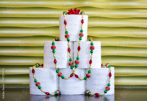 a pyramid of toilet paper decorated with colorful, sparkly Christmas beads against a gold background with copy space