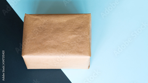Parcel on coloured background, copy space. Blank box wrapped in kraft paper. Delivery service concept.