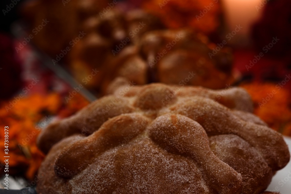 Pan de Muerto sugared, placed on a glass plate, around marigold flowers, burning candles, in the background traditional pan de Muerto