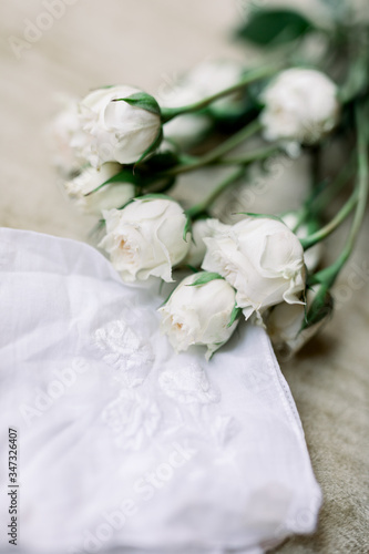 A bouquet of white roses lying on top of an embroidered white handkerchief. This is a wedding day detail. 