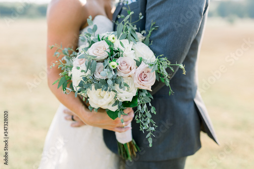 Bride and Groom Together with Bride Holding a White and Dusty Pink Rose Bridal Bouquet with Green Olive Leaves. 