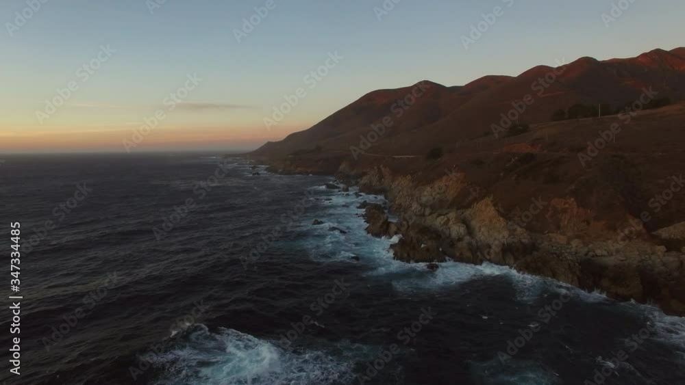 Aerial: Waves splashing on rocks in sea against sky during sunset, scenic view of mountains - Big Sur, California Aerial: Waves splashing on rocks in sea against sky during sunset, scenic view of mountains - Big Sur, California