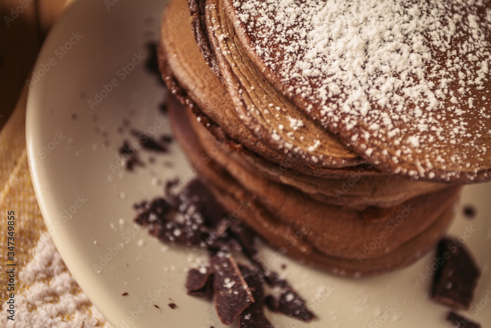 Fototapeta premium A view of delicious cocoa pancakes with dark chocolate and powdered sugar on a wooden table