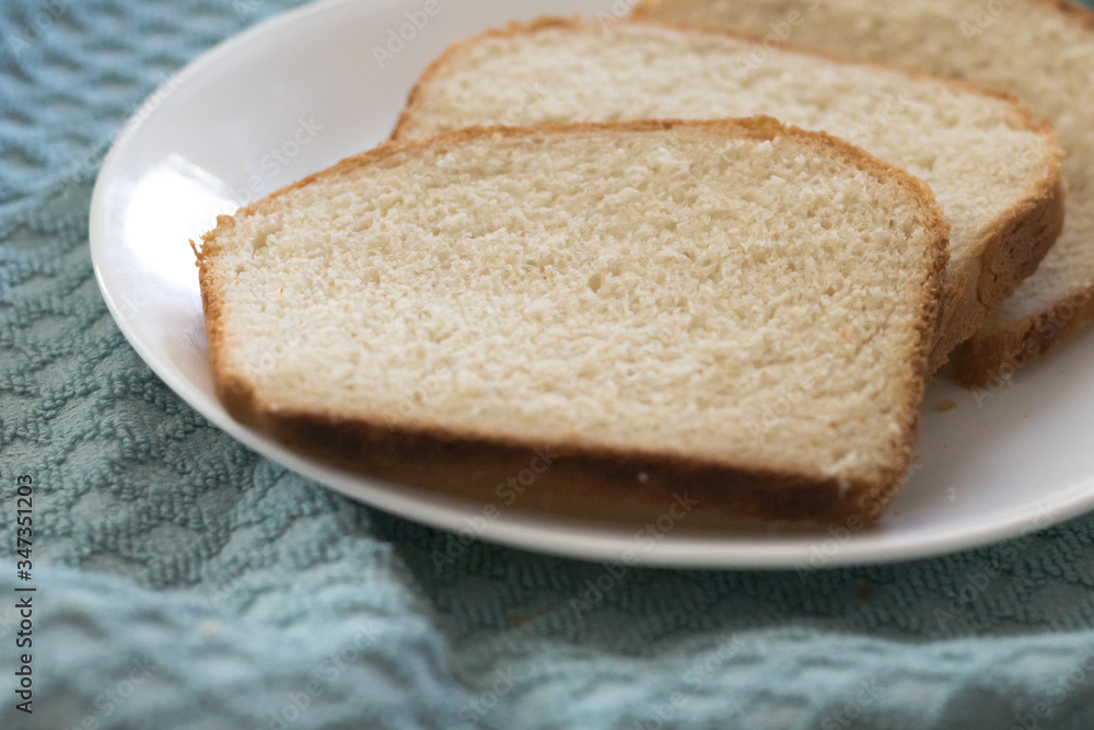 Sliced of freshly, homemade white bread on a white plate with a textured blue cloth background.