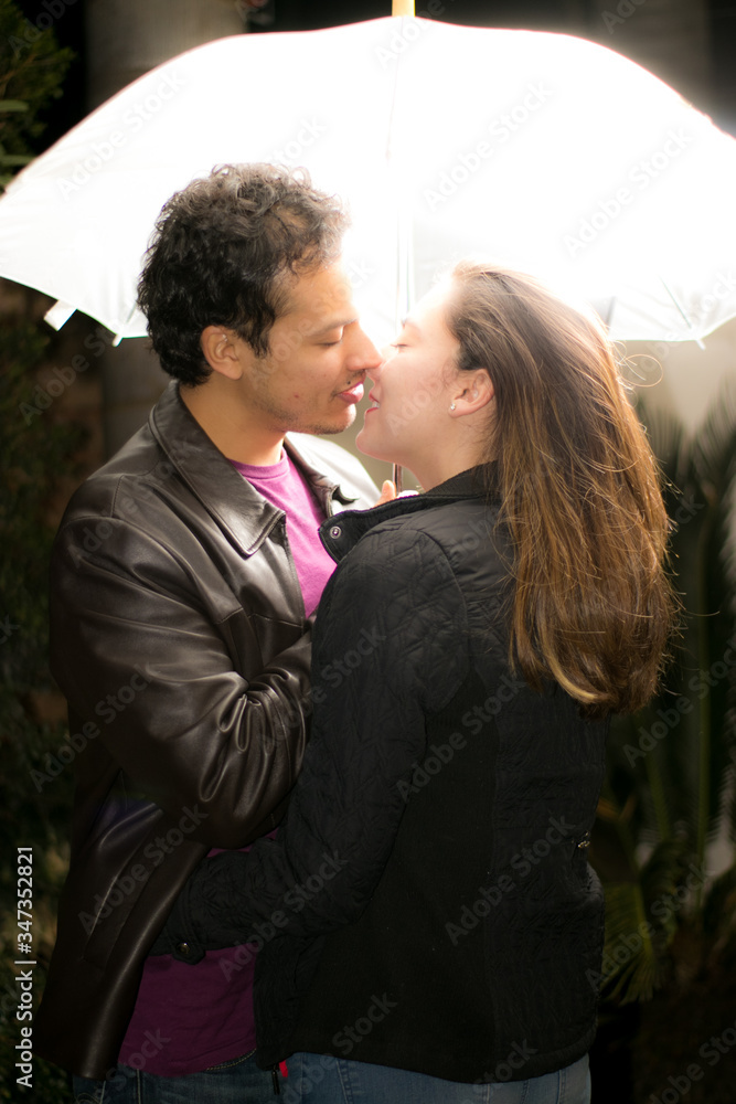 Pareja de novios a punto de darse un beso pajo un paraguas Pareja de novios a punto de darse un beso pajo un paraguas