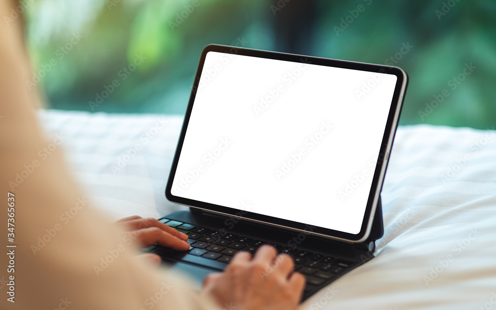 Mockup image of a woman using and typing on tablet pc with blank white desktop screen as computer pc while lying down on a cozy white bed at home Mockup image of a woman using and typing on tablet pc with blank white desktop screen as computer pc while lying down on a cozy white bed at home