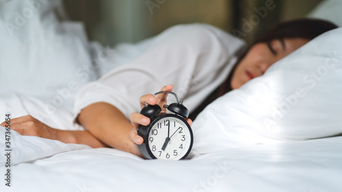Photography An asian woman turning off an alarm clock while sleeping on a white cozy bed in