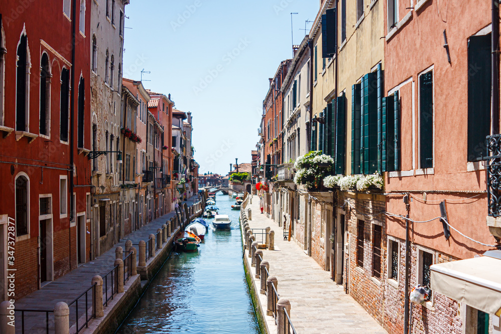 Cityscape with ancient buildings with flowers on their balconies on both sides of the canal in Venice, Italy.
