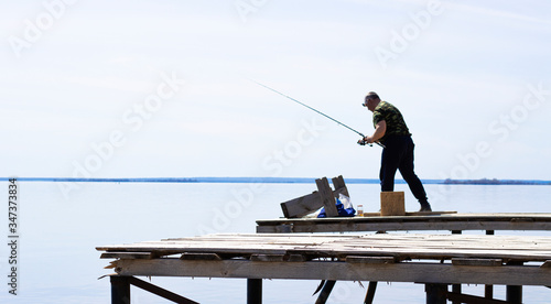 a lone fisherman catches fish from a wooden pier on the banks of the Kama river