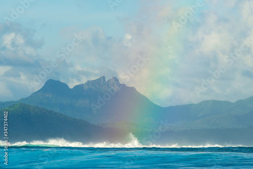 A huge rainbow against the backdrop of picturesque mountains, waves and ocean. Mauritius Island, Indian Ocean