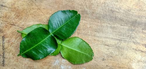 Two kaffir lime leaves, one upside down and the other face up on the wood floor.