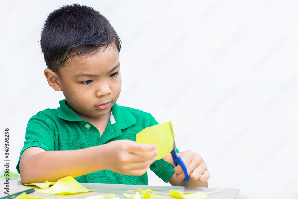 Portrait image of 5-6 years old Asian child boy practice to cutting color paper by the scissors on the wooden table.Study from home, social Distancing, Kid and education concept. Portrait image of 5-6 years old Asian child boy practice to cutting color paper by the scissors on the wooden table.Study from home, social Distancing, Kid and education concept.