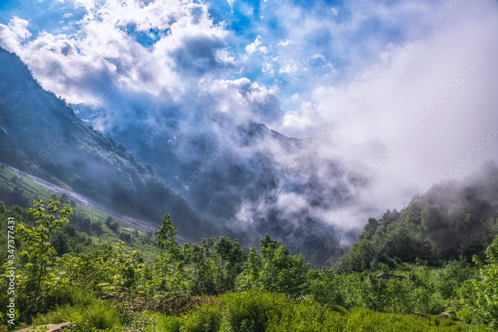 Heavy fog and clouds in mountain gorge in the summer or spring. A layer of melting snow in the summer in high mountains. Heavy fog and clouds in mountain gorge in the summer or spring. A layer of melting snow in the summer in high mountains.