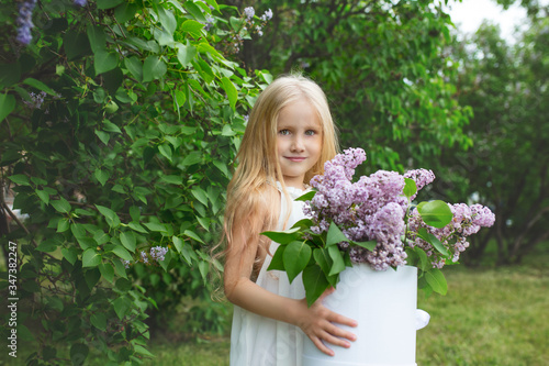 Small and beautiful girl child cute and happy with lilac flowers in her hands in nature