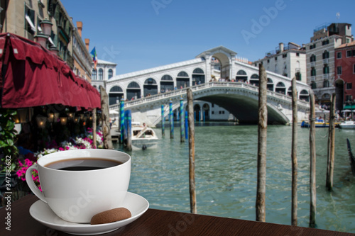 Cup of back coffee or tea with cookie with view on famous Canal Grande and Rialto Bridge in Venice, Italy