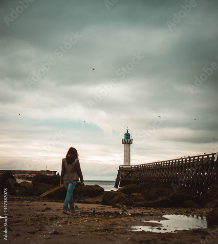 young woman walking on the beach towards a lighthouse
