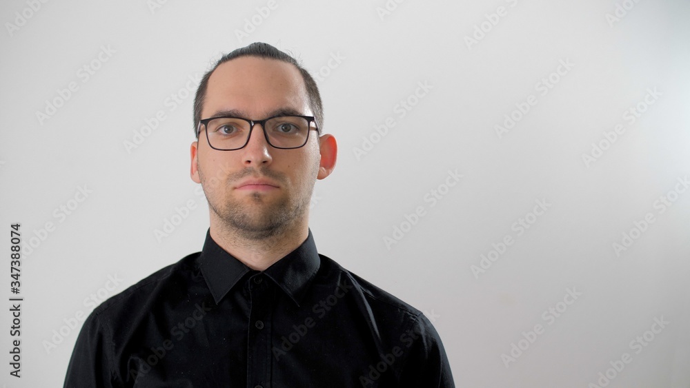 Obraz premium Portrait serious face of young man in glasses with black hair close up. Cute man looks positive. Bearded handsome man in a black shirt looking to camera. Confident attractive close up confidence. 