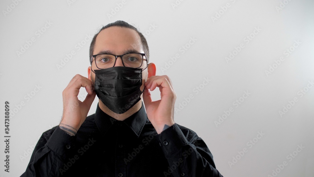 Man puts on medical mask. Attractive man shows how to wear a medical mask. Portrait of adult european guy wearing medical mask during coronavirus. Virus prevention coronavirus concept. Man puts on medical mask. Attractive man shows how to wear a medical mask. Portrait of adult european guy wearing medical mask during coronavirus. Virus prevention coronavirus concept.
