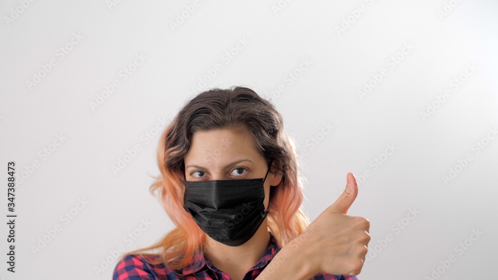 Woman shows thumb at camera. Portrait of adult european girl wearing medical protective black face mask during coronavirus. Virus prevention. Health care and medical concept. Woman shows thumb at camera. Portrait of adult european girl wearing medical protective black face mask during coronavirus. Virus prevention. Health care and medical concept.