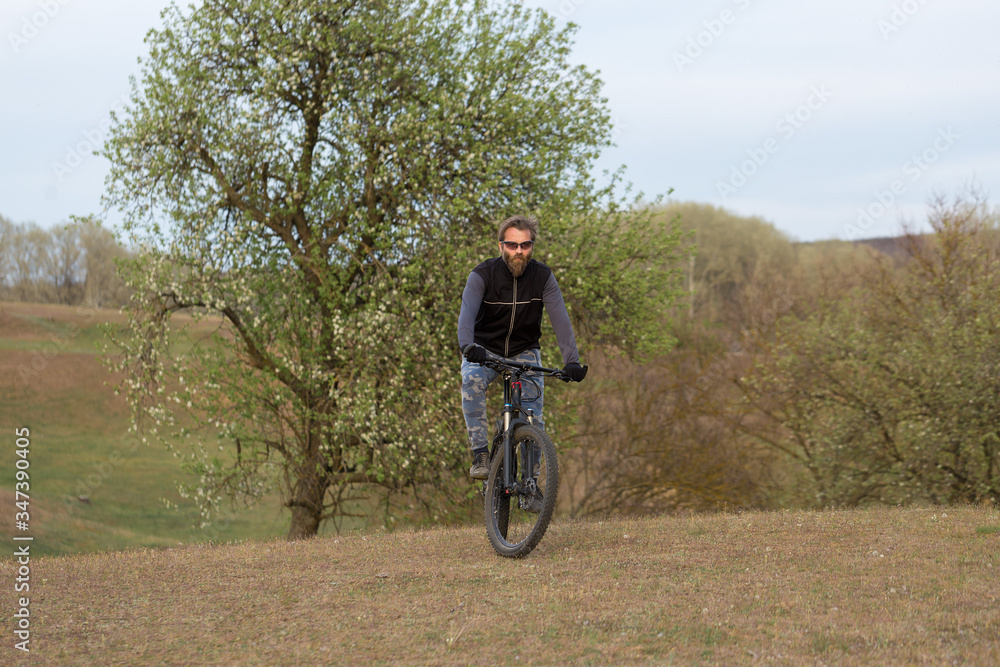 Sports brutal bearded guy on a modern mountain bike. Cyclist on the green hills in the spring. Sports brutal bearded guy on a modern mountain bike. Cyclist on the green hills in the spring.