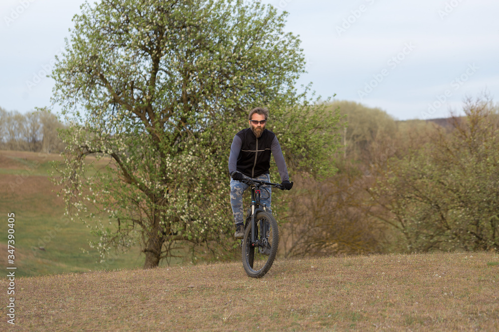 Sports brutal bearded guy on a modern mountain bike. Cyclist on the green hills in the spring.