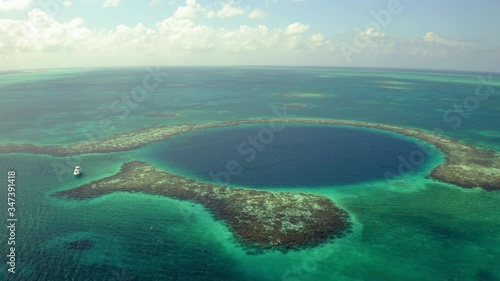 Aerial: Yacht near sinkhole against sky on sunny day, scenic view of seascape while drone panning from left to right - Great Blue Hole, Belize