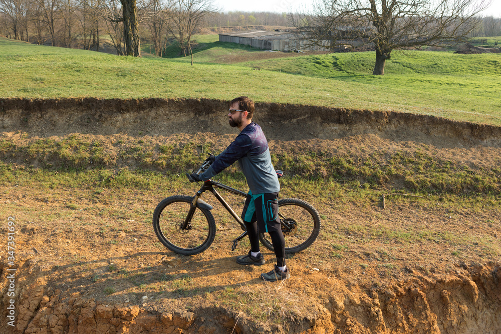 Cyclist in shorts and jersey on a modern carbon hardtail bike with an air suspension fork standing on a cliff against the background of fresh green spring forest Cyclist in shorts and jersey on a modern carbon hardtail bike with an air suspension fork standing on a cliff against the background of fresh green spring forest