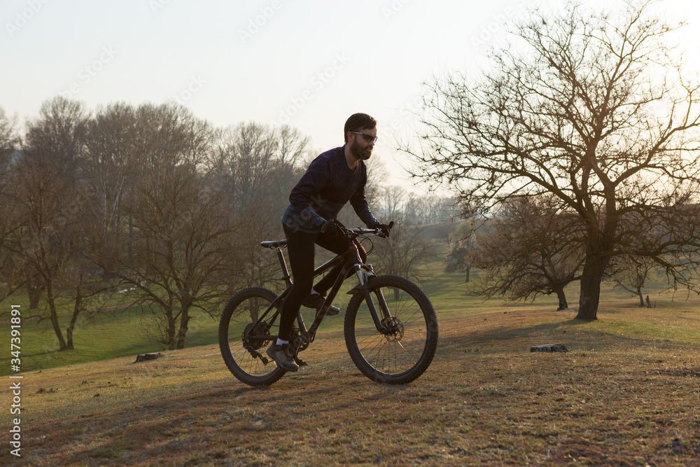 Cyclist in shorts and jersey on a modern carbon hardtail bike with an air suspension fork standing on a cliff against the background of fresh green spring forest