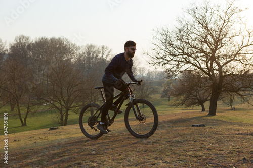 Cyclist in shorts and jersey on a modern carbon hardtail bike with an air suspension fork standing on a cliff against the background of fresh green spring forest