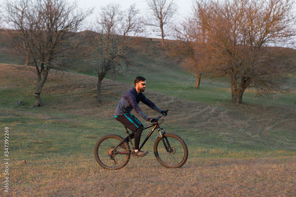 Cyclist in shorts and jersey on a modern carbon hardtail bike with an air suspension fork standing on a cliff against the background of fresh green spring forest