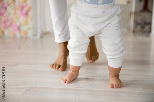 Crop close up of young biracial mom hold little infant toddler learn walking at home, small baby do make first steps with african American mother support and care, upbringing, maternity concept photo